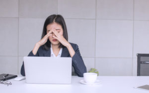 woman sitting at her desk is fighting a headache and neck pain