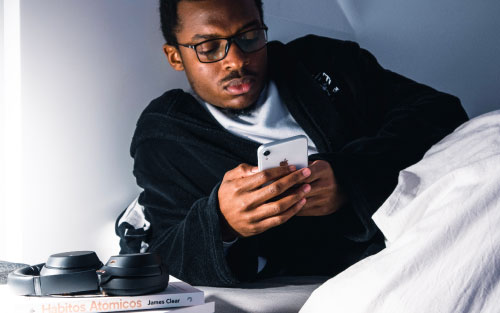 man with glasses scrolling his phone in bed at night